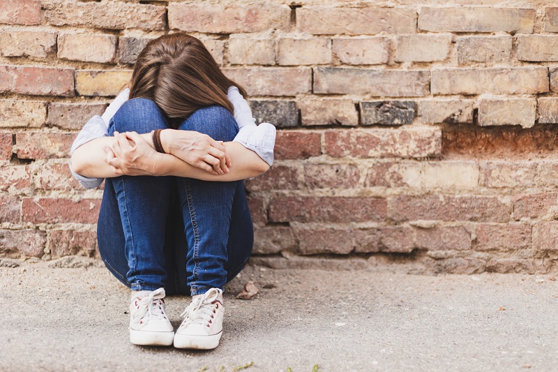 sad teen sitting against brick wall