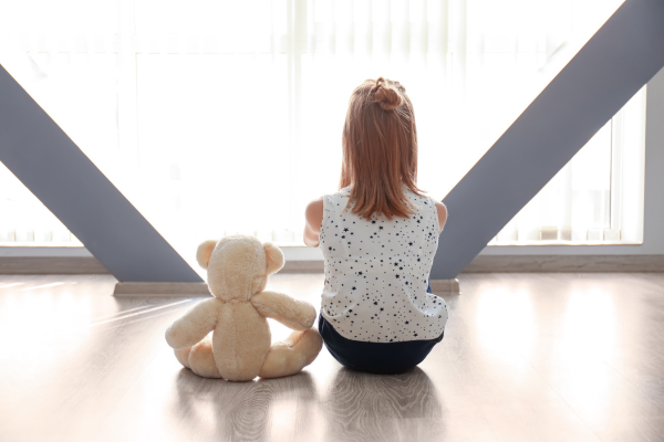 Autistic girl with back to camera sitting with toy bear