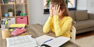 A young who has an open school book in front of her and girl covering her face with her hands