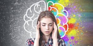 Student closing eyes with fingers on temples in front of colorful black board