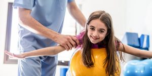 Girl at occupational therapy leaning on a ball smiling at camera